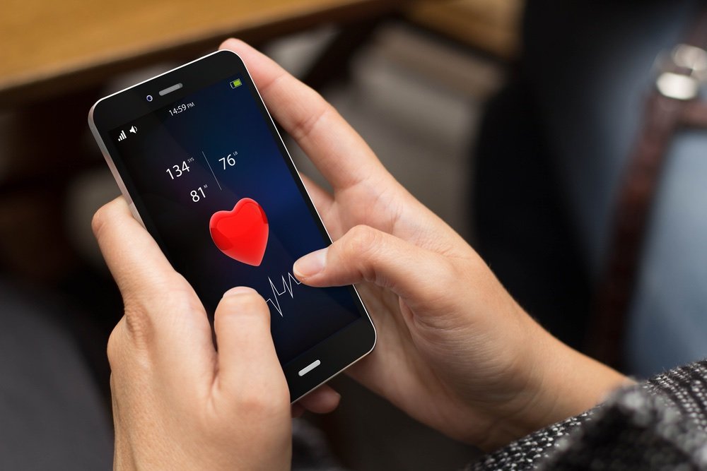 Frau hält ein Smartphone mit der Anzeige einer Herzfrequenz App